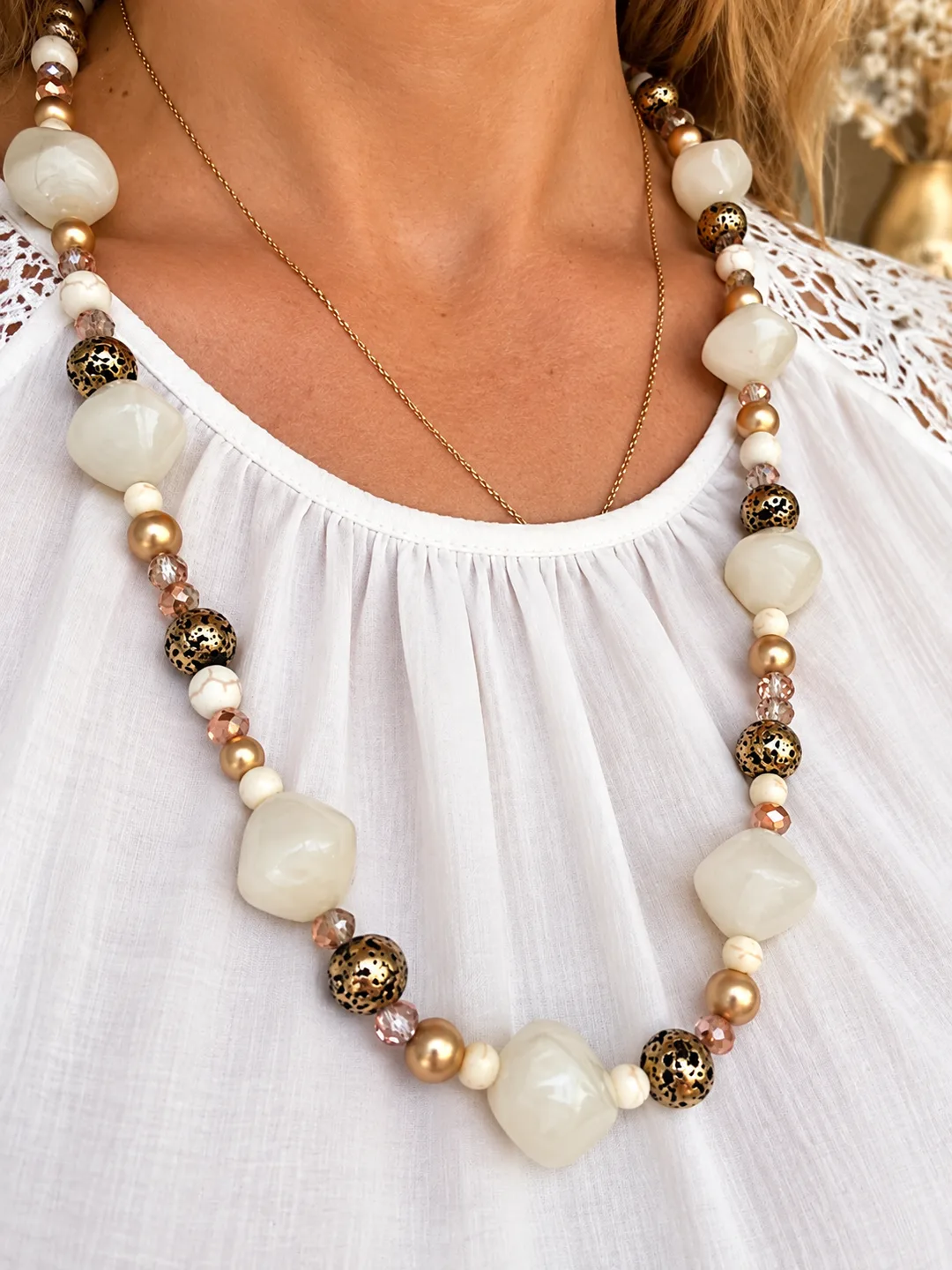 Collier de perles crème nacrées, dorées et bronze moucheté porté sur une blouse blanche